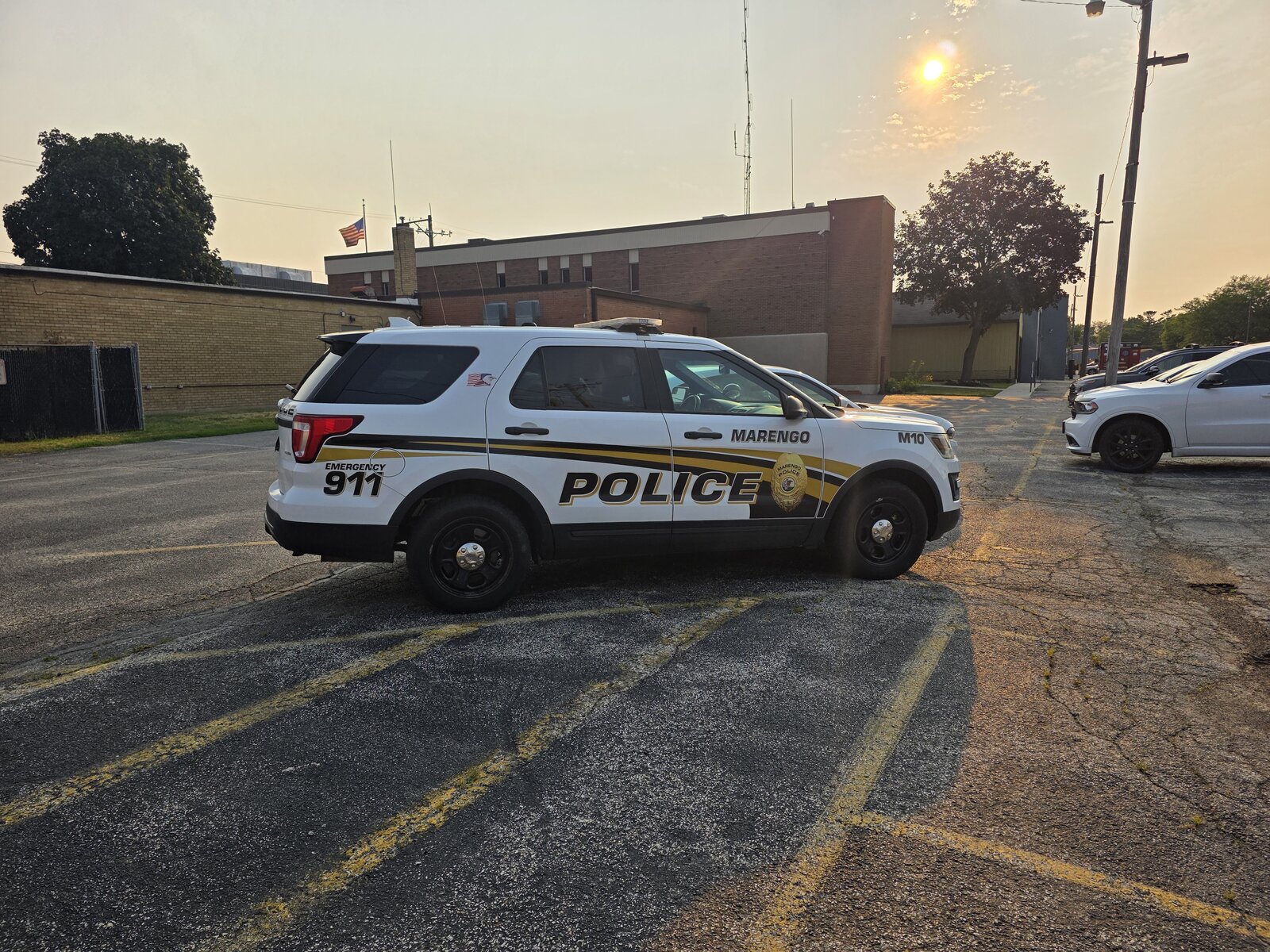 A Marengo Police SUV, unit M10, parked outside the police department building at dusk, an American flag flying behind it.